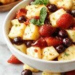 A colorful summer fruit salad in a glass bowl with sliced strawberries, blueberries, pineapple chunks, and kiwi slices garnished with mint leaves