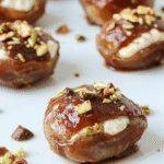 A close-up of plump dates filled with creamy ricotta cheese, topped with crushed pistachios and drizzled with honey, on a rustic wooden platter.