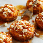 Colorful close-up of golden-brown sweet potato rounds topped with crumbled white feta cheese and a drizzle of glossy honey, garnished with fresh herbs, arranged on a rustic plate with a textured background emphasizing textures and vibrant colors.